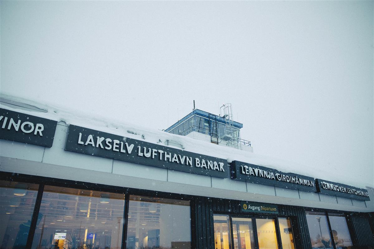 Fasaden til en flyplass. På fasadens skilt kan man lese "Lakselvlufthavn Banak". Bildet er tatt på vinterstid, det snør. - Klikk for stort bilde