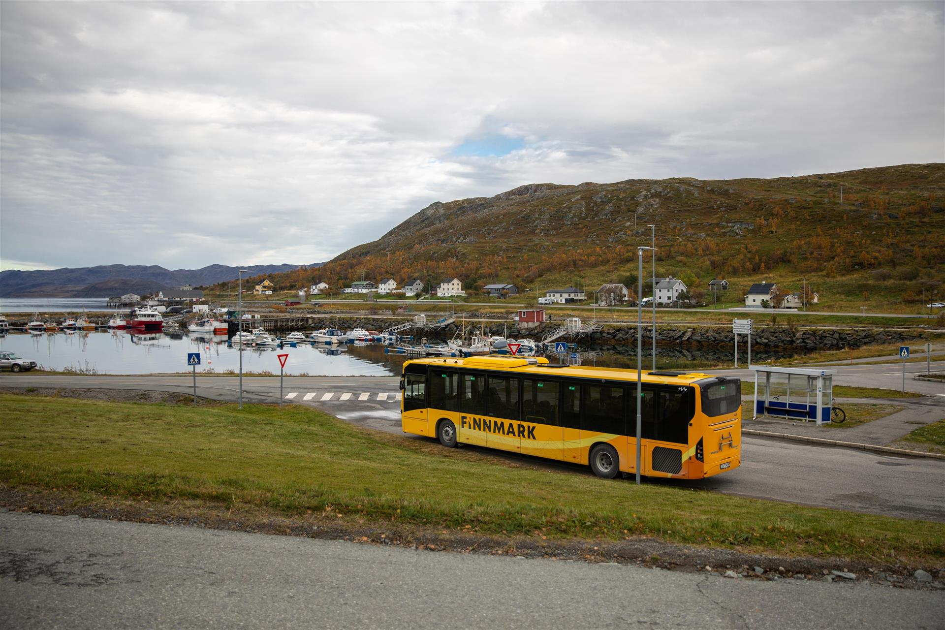 En gul Snelandiabuss står parkert på en bussholdeplass i Kvalsund sentrum, Hammerfest kommune.