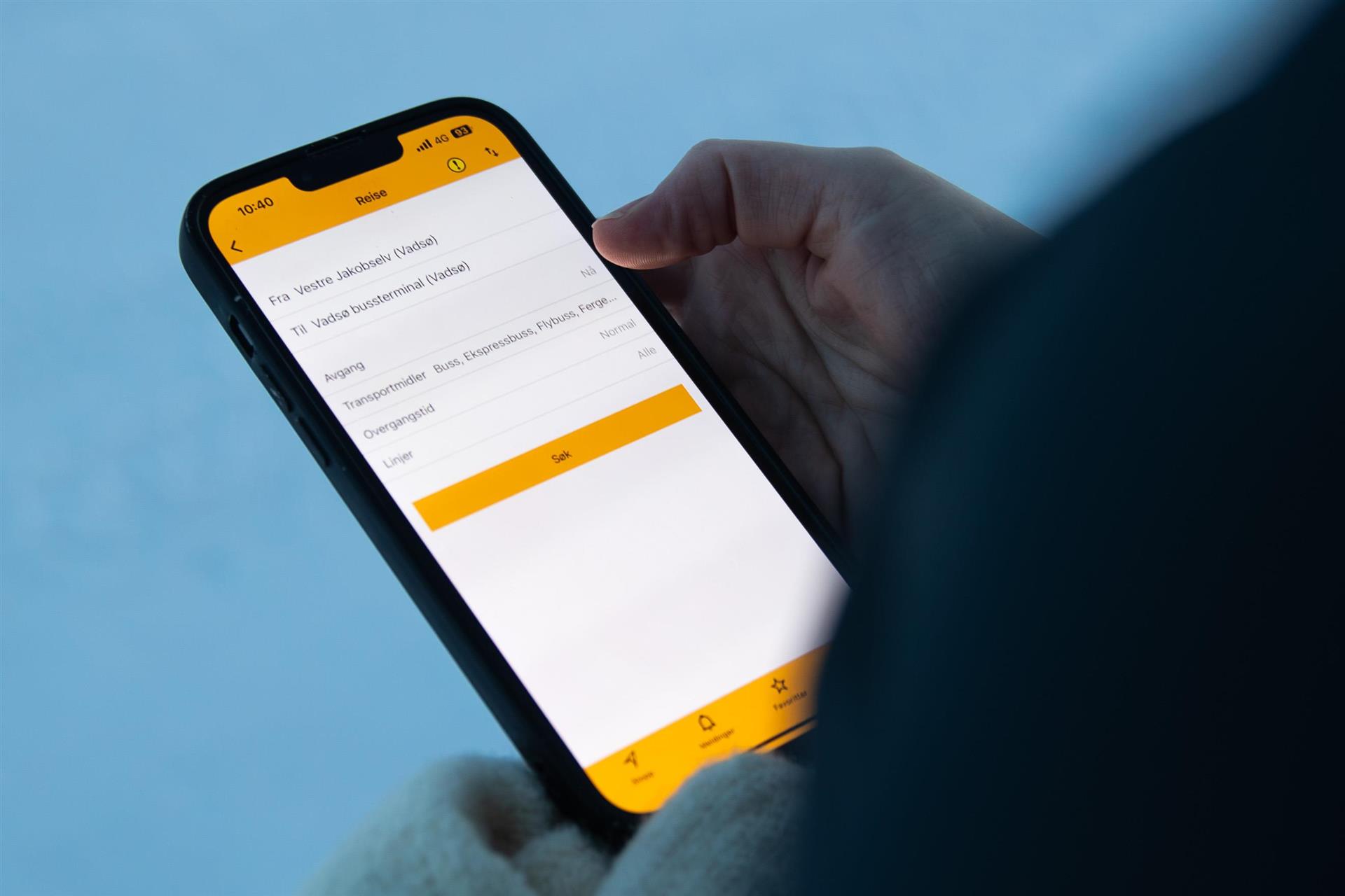 Bilde av en person som holder en smarttelefon med en reiseplanlegger-app aktiv. Bildet er tatt på vinterstid.